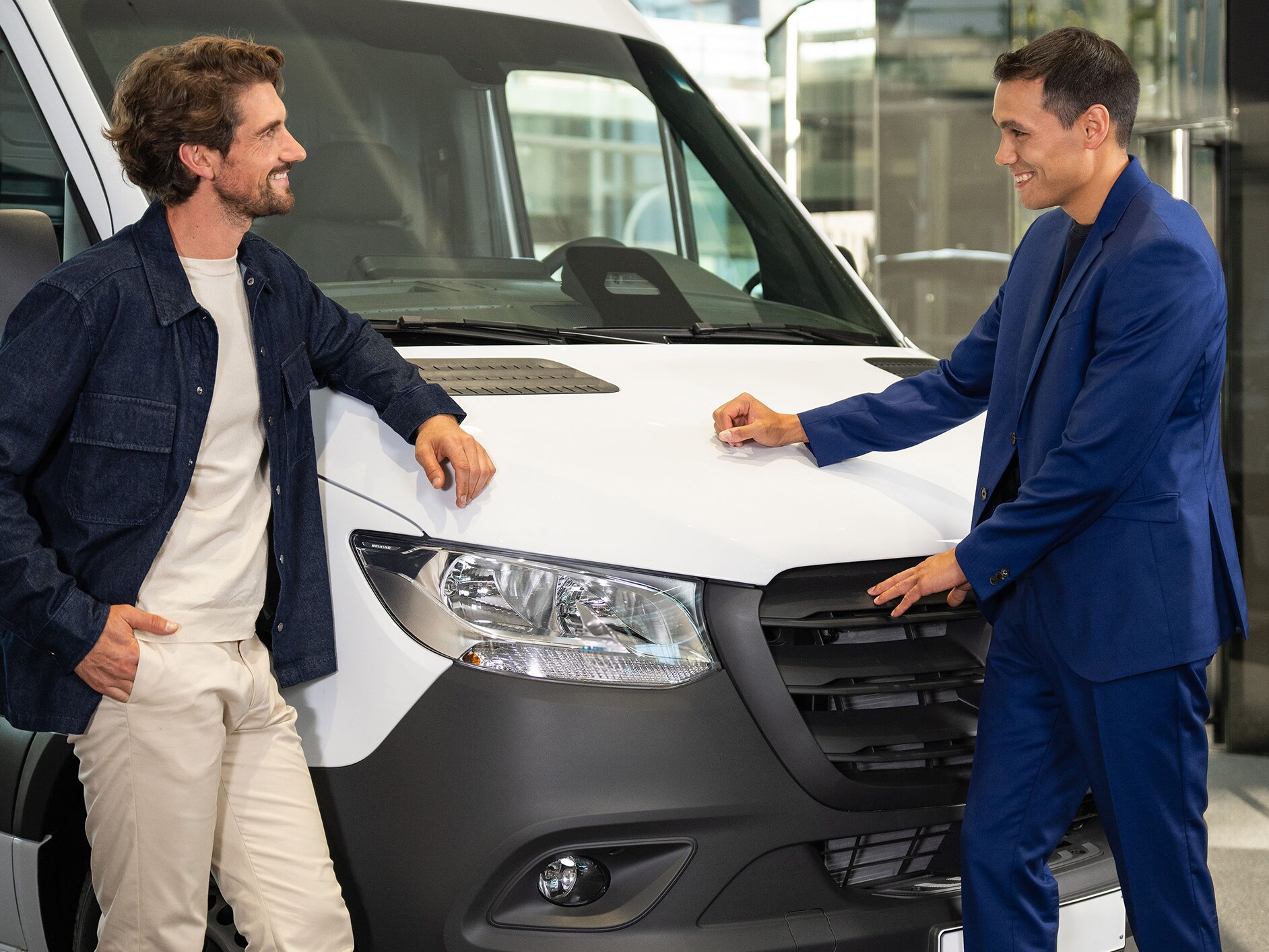 Deux personnes discutent et pointent vers un appareil mobile tout en se tenant devant un utilitaire Mercedes-Benz.