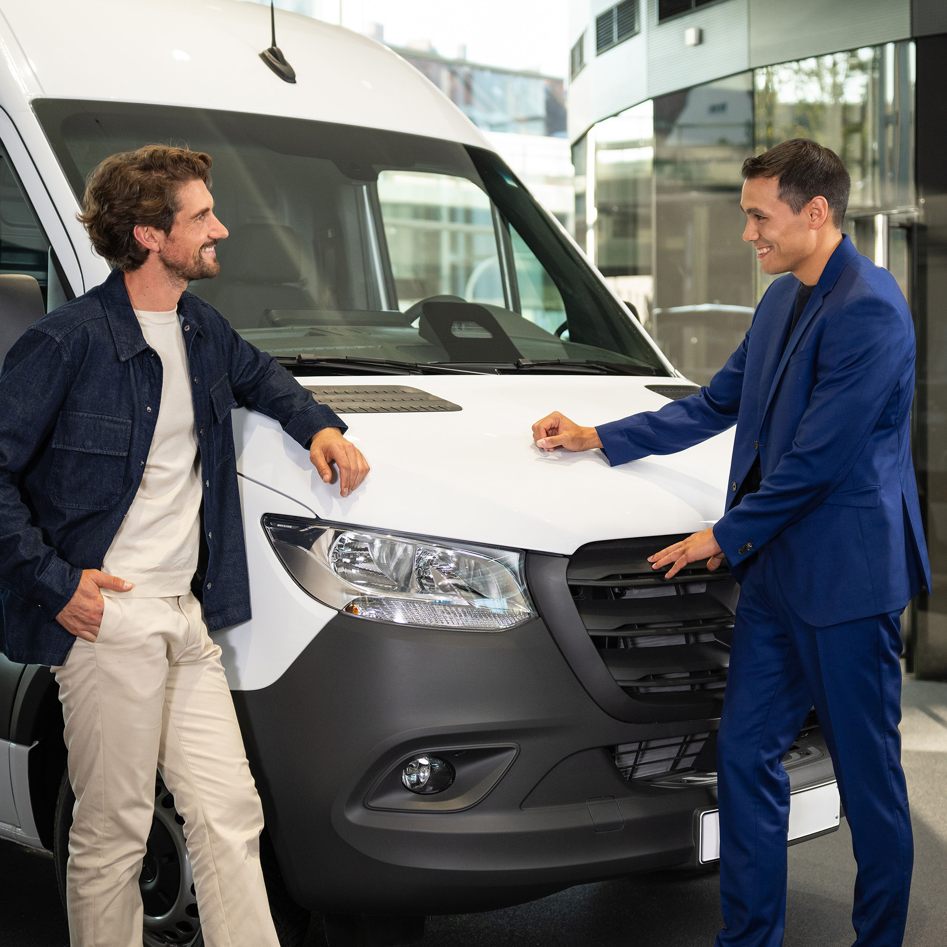 Kunde bespricht einen Transporter mit einem Berater Kunde im Gespräch mit einem Berater neben einem weißen Mercedes-Benz Transporter im Showroom.