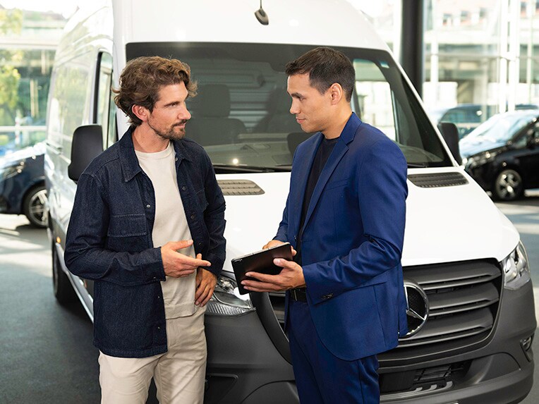 Client en discussion avec un conseiller à côté d'un véhicule utilitaire Mercedes-Benz blanc dans le showroom.