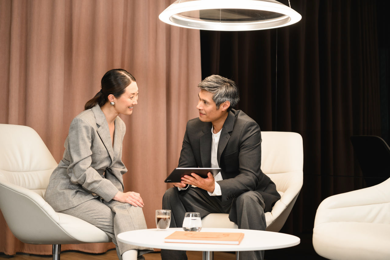 Entretien avec un client dans un espace d'accueil moderne. Deux clients professionnels discutent des possibilités en matière de véhicules utilitaires dans un espace lounge confortable.