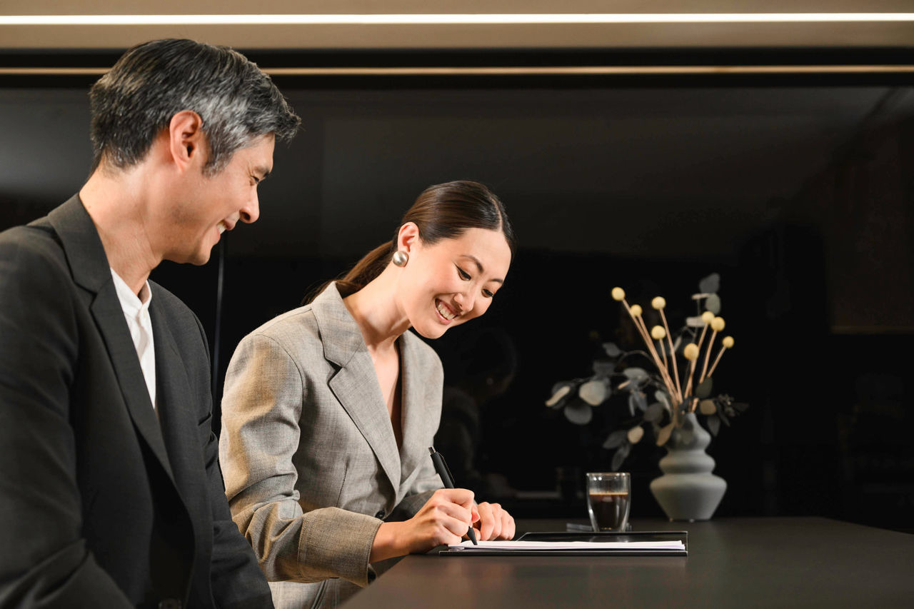 Client professionnel signant un contrat pour un véhicule utilitaire. Un client signe des documents lors d'un entretien avec un conseiller Mercedes-Benz dans un espace d'accueil confortable.