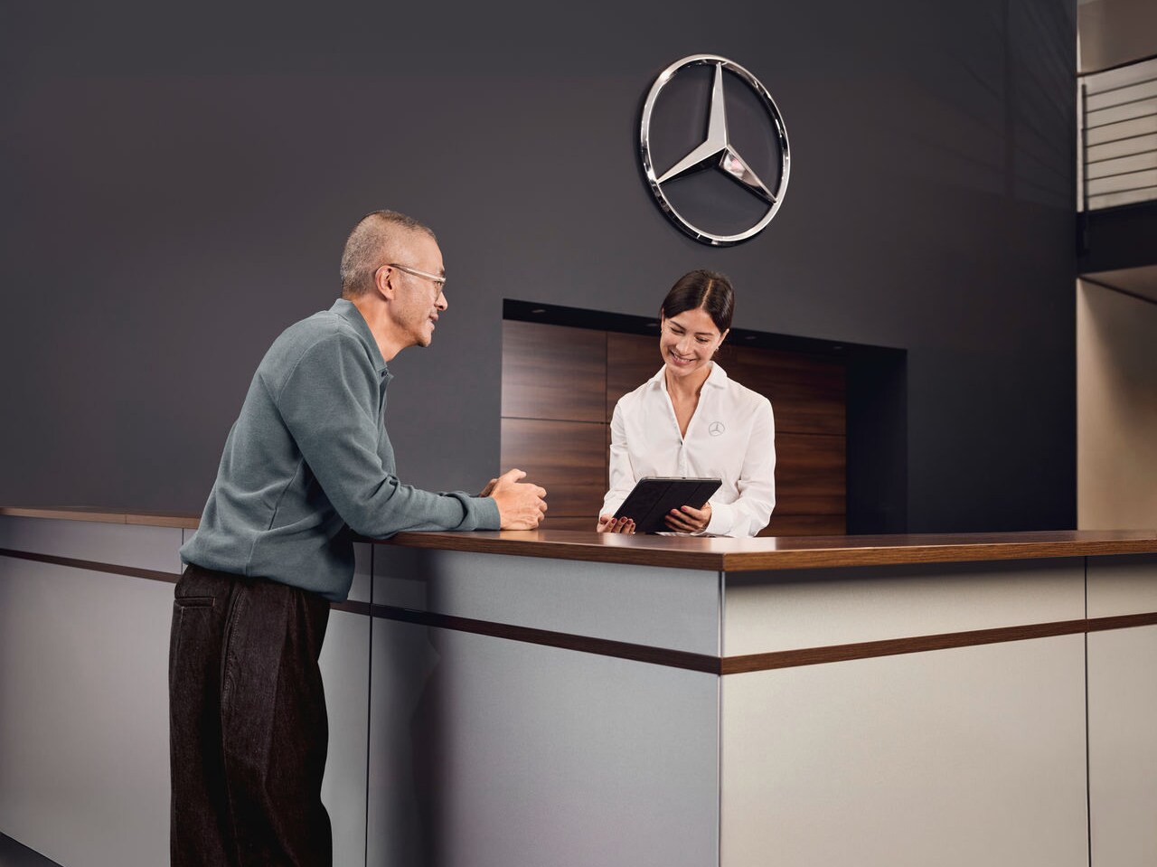 Un client est accueilli et assisté par un collaborateur au comptoir de réception d'une concession Mercedes-Benz.