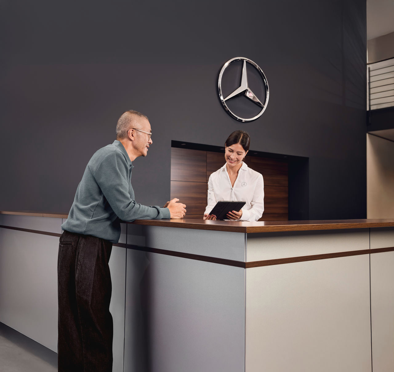 Client recevant de l'assistance à la réception Mercedes-Benz. Un client est accueilli et assisté par un collaborateur au comptoir de réception d'une concession Mercedes-Benz.