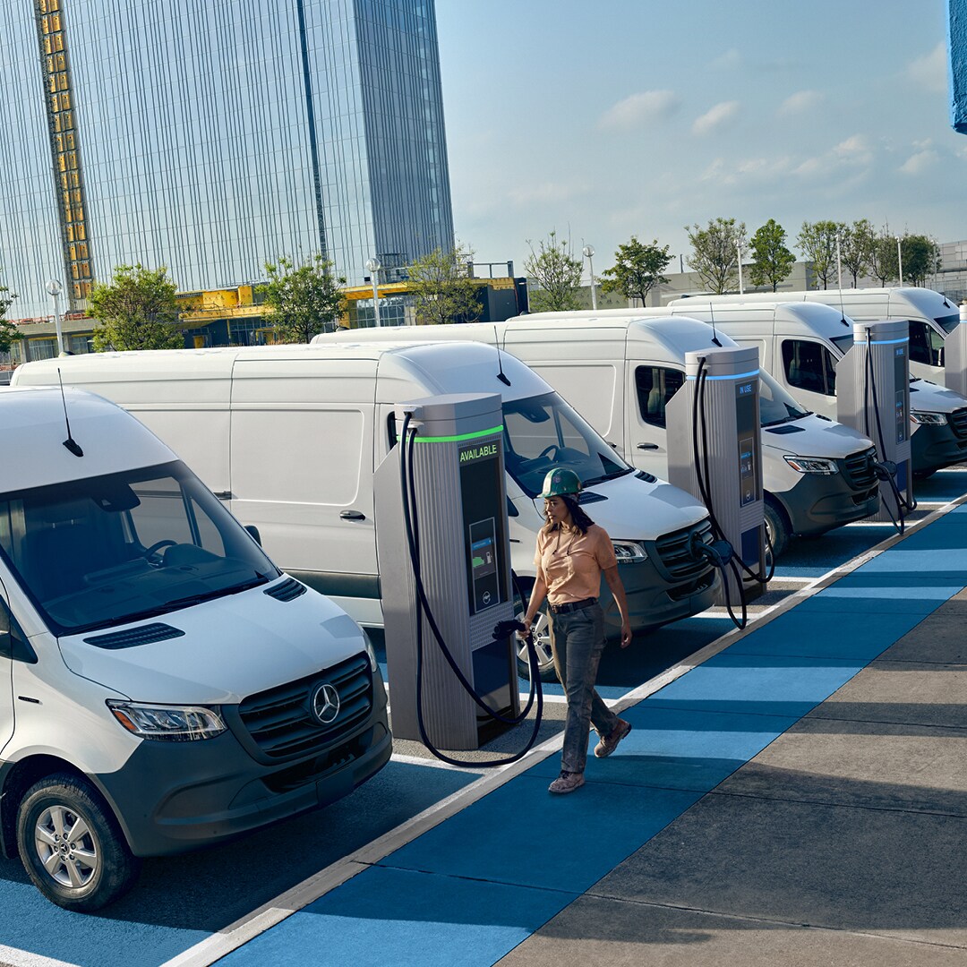 The Mercedes-Benz Sprinter Panel Van is driving on the street in front of a building.   